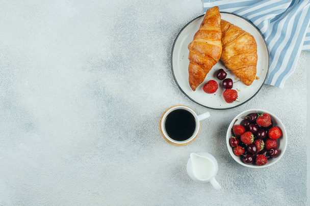 Food background. Coffee, croissants and berries for breakfast on light concrete background. Top view with copy space - Фото, изображение