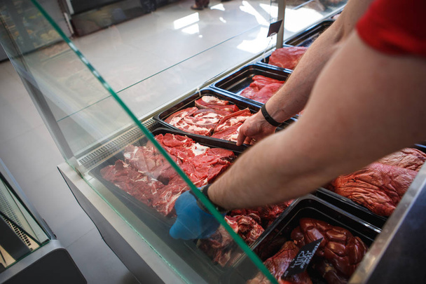 Raw meat in trays in the window of a butcher shop. The seller puts the meat on display in black trays - Φωτογραφία, εικόνα