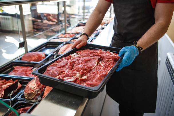 Raw meat in trays in the window of a butcher shop. The seller puts the meat on display in black trays - Photo, image