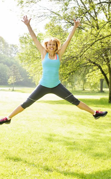 Smiling woman jumping in park - Foto, imagen