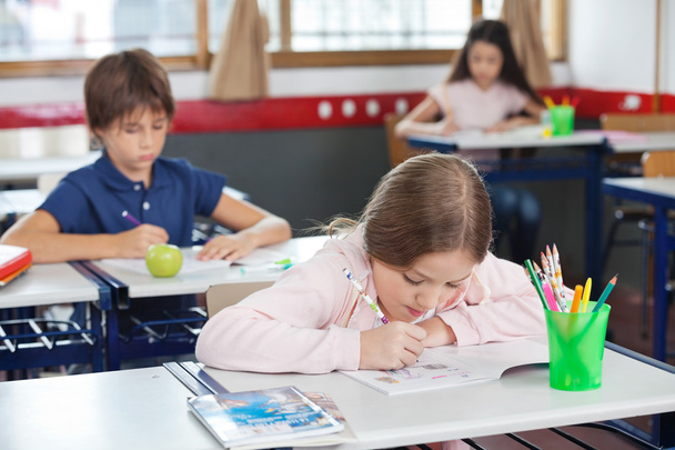 Schoolgirl Drawing While Leaning On Desk In Classroom - Photo, Image