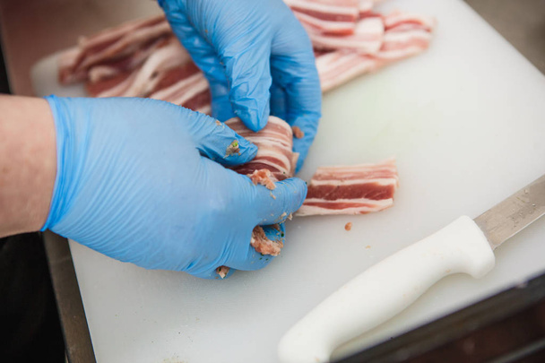 The process of preparing meat products. Gloved hands are molded from ground beef and bacon patties - Фото, изображение