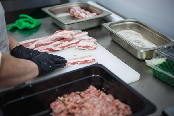 The process of preparing meat products. Gloved hands are molded from ground beef and bacon patties - Foto, Imagen