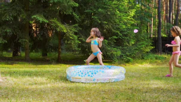 zwei kleine Mädchen spielen im Sommer am Pool mit Wasserballons - Filmmaterial, Video