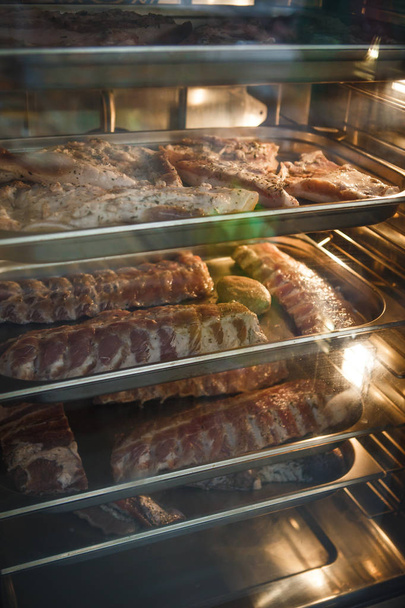 Smoked meat products in the oven smokehouse. A man holding a tray of smoked meat products - Photo, image