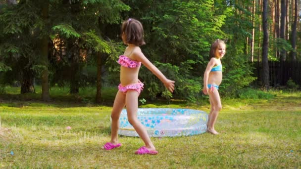zwei kleine Mädchen spielen im Sommer am Pool mit Wasserballons - Filmmaterial, Video