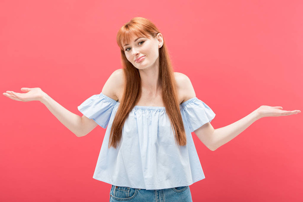 surprised redhead girl showing shrug gesture and looking at camera isolated on pink - Fotoğraf, Görsel