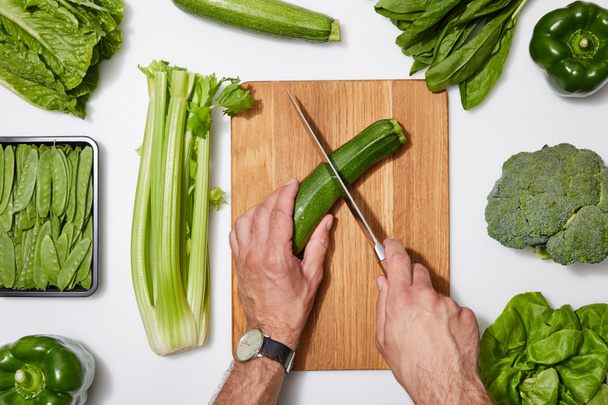 top view of man cutting green vegetables on wooden chopping board white background - Foto, immagini