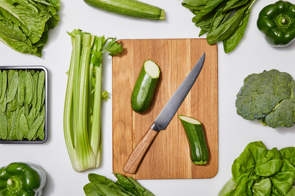 ylhäältä näkymä vihreitä vihanneksia ja leikkuulauta veitsellä valkoisella taustalla
 - Valokuva, kuva