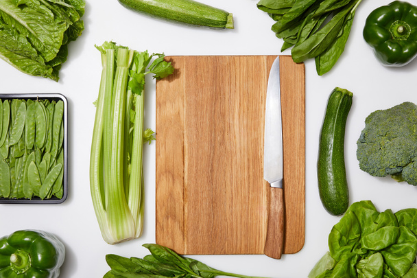 ylhäältä näkymä vihreitä vihanneksia ympärillä puinen leikkuulauta veitsi valkoisella pohjalla
 - Valokuva, kuva
