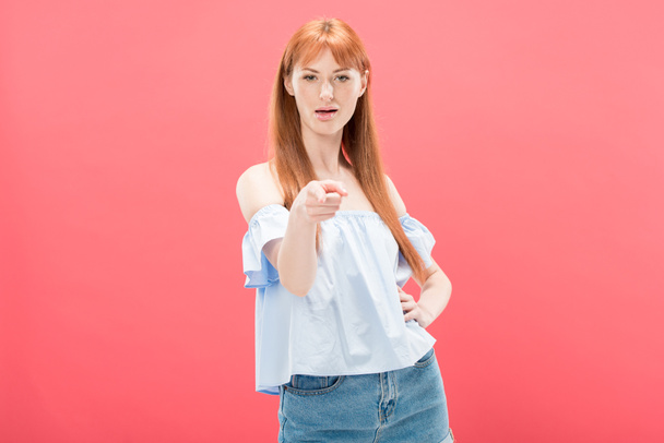 redhead woman standing with hand on hip and pointing with finger at camera isolated on pink - Фото, зображення