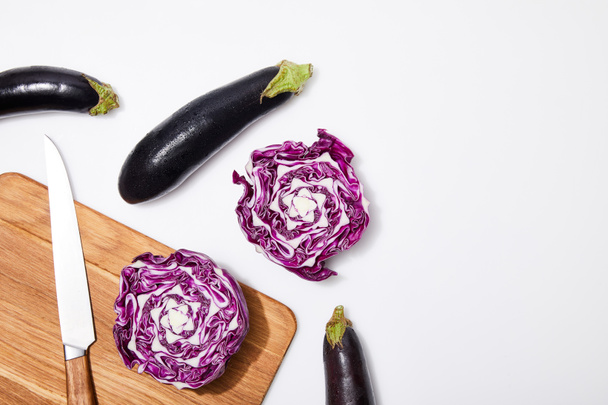 top view of red cabbage and eggplants on wooden chopping board and knife on white background - Foto, Bild