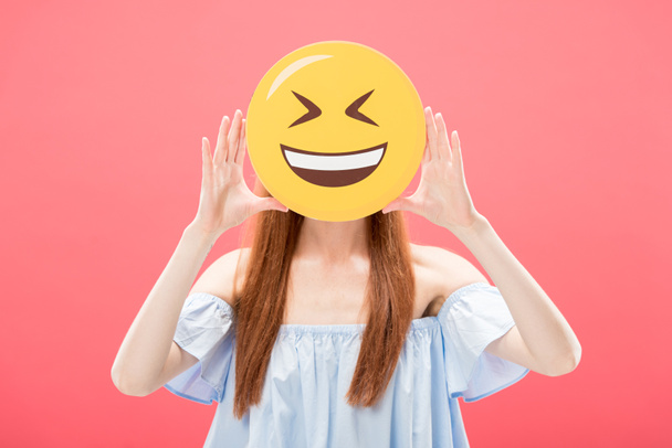 KYIV, UKRAINE - MAY 23, 2019: front view of redhead girl holding laughing smiley isolated on pink - Photo, image