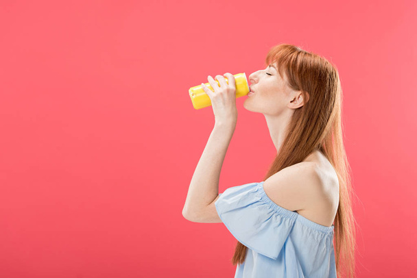 side view of redhead girl drinking beverage isolated on pink - 写真・画像