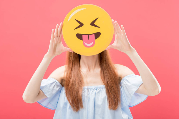 KYIV, UKRAINE - MAY 23, 2019: front view of redhead girl holding laughing smiley isolated on pink - Foto, Imagem
