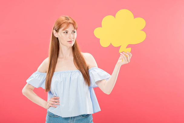 attractive redhead young woman standing with hand on hip and holding empty thought bubble isolated on pink - Photo, Image