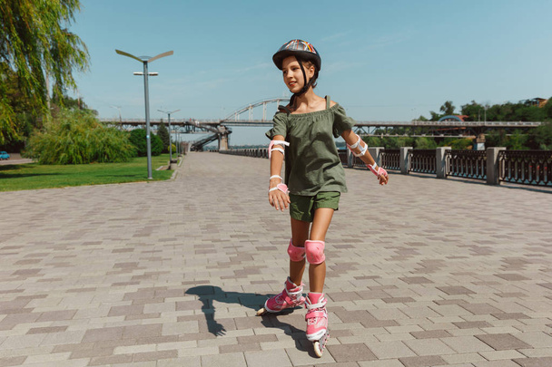 Teenage girl in a helmet learns to ride on roller skates outdoors - Foto, immagini