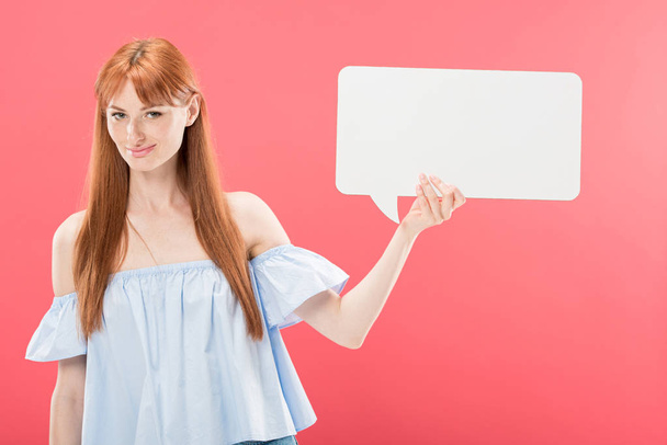 smiling attractive redhead girl holding empty speech bubble isolated on pink - Фото, зображення