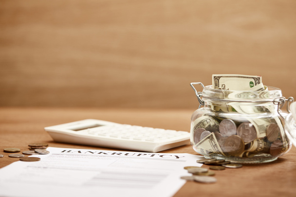 selective focus of bankruptcy form, coins, calculator and glass jar with dollar banknotes - Foto, immagini