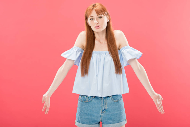 redhead young woman looking at camera and showing shrug gesture isolated on pink - Photo, Image