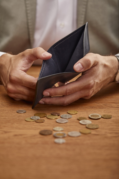 περικομμένη όψη του ανθρώπου δείχνοντας άδειο πορτοφόλι κοντά σε κέρματα σε ξύλινο τραπέζι - Φωτογραφία, εικόνα
