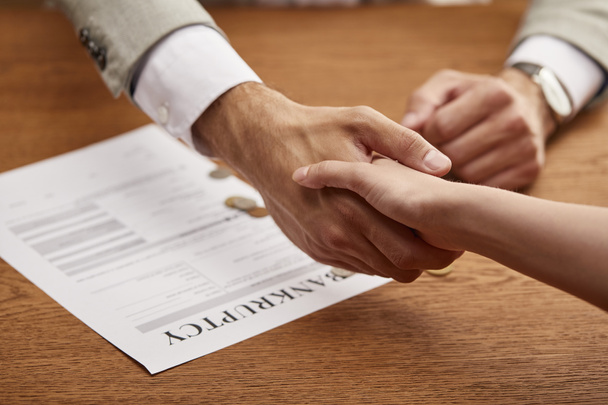 partial view of man and woman shaking hands near bankruptcy form - Photo, Image