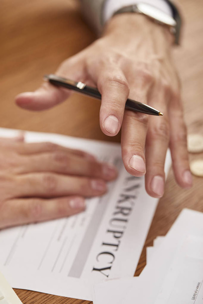 cropped view of businessman holding pen above bankruptcy form at wooden table - Foto, afbeelding