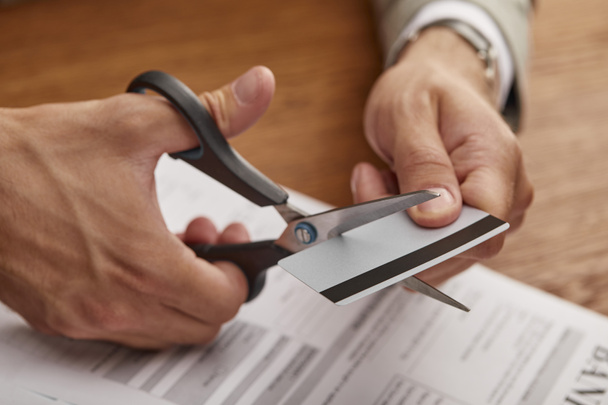 partial view of businessman cutting credit card with scissors at wooden table  - Foto, Bild