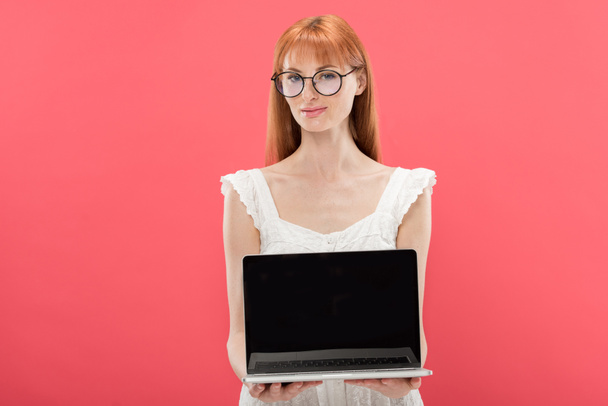 rousse jeune femme dans des lunettes tenant ordinateur portable avec écran blanc isolé sur rose
 - Photo, image