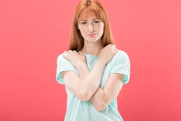 front view of upset redhead girl in t-shirt looking at camera isolated on pink - 写真・画像