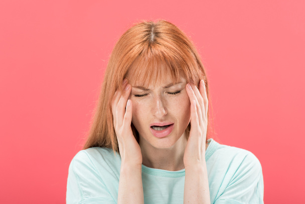 front view of young redhead woman in t-shirt with headache touching head isolated on pink - Foto, Imagen