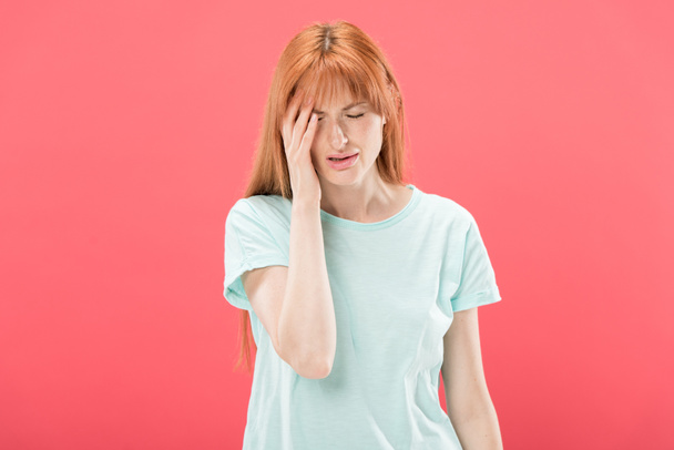 front view of young redhead woman in t-shirt with headache touching head isolated on pink - Photo, Image