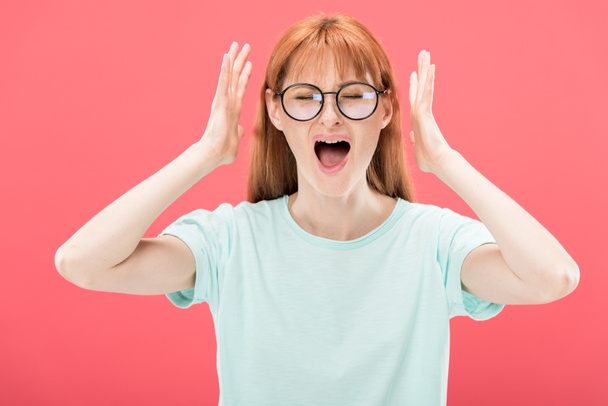 front view of angry redhead woman in glasses screaming with closed eyes and t-shirt isolated on pink - Photo, Image