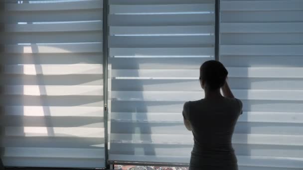 女性は、パノラマの街の景色とストレッチで窓を見て、ブラインドを開いています. - 映像、動画