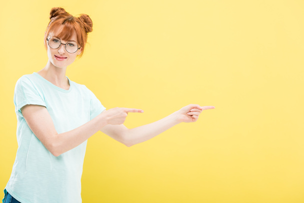 punapää tyttö lasit ja t-paita osoittaa sormilla eristetty keltainen
 - Valokuva, kuva