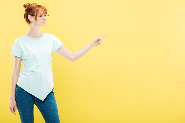 redhead girl in glasses and t-shirt pointing with finger isolated on yellow - Photo, Image