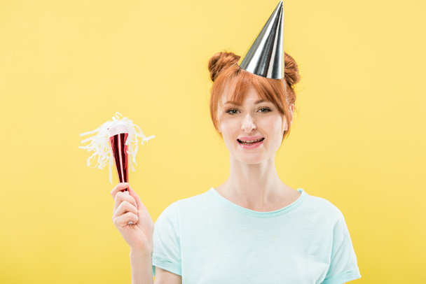 front view of excited redhead birthday girl in party cap smiling isolated on yellow - Zdjęcie, obraz