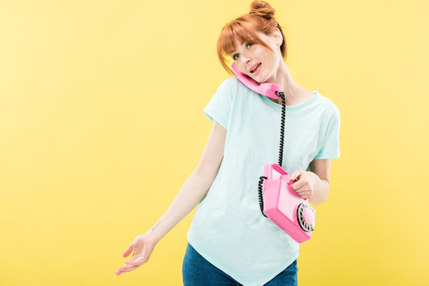 привлекательная рыжая молодая женщина разговаривает по ретро-телефону изолированы на желтый
 - Фото, изображение