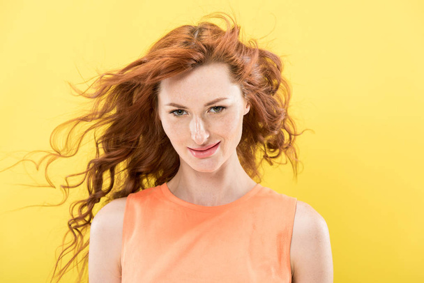 front view of smiling curly redhead woman looking at camera isolated on yellow - Photo, image