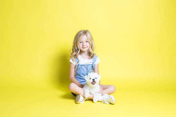 Cute little girl with her puppy on yellow background. - Фото, изображение