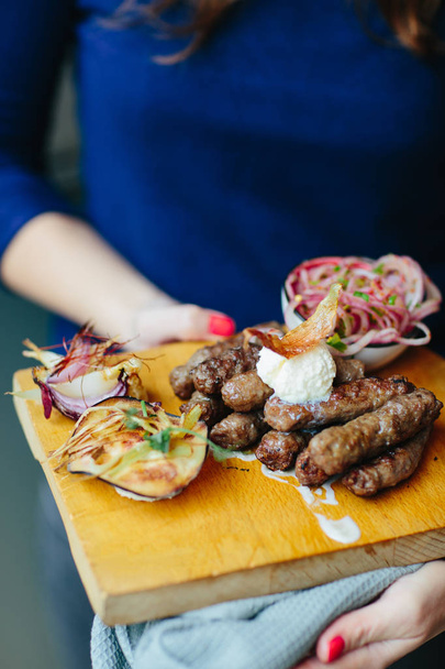 cropped shot of woman holding wooden board with Cevapi, cevapcici, traditional Balkan food. Minced meat prepared on grill - Fotografie, Obrázek