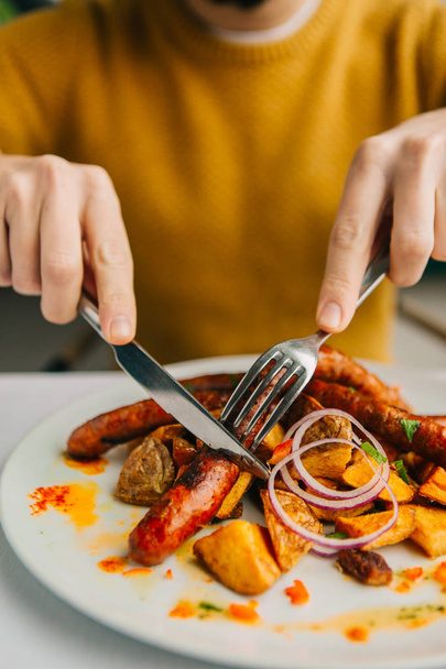 cropped shot of person holding fork with knife and eating delicious sausages - Foto, Imagem