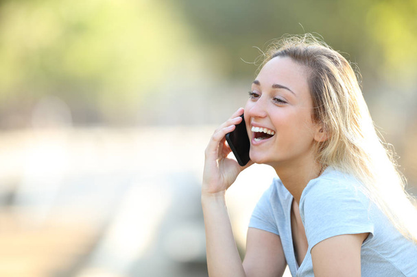 Happy teenage girl talking on phone in a park - Photo, Image