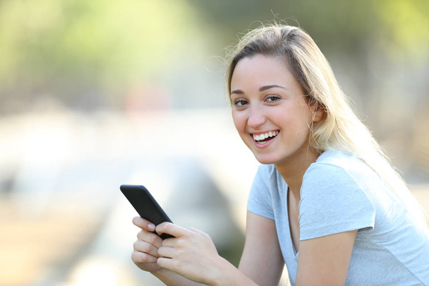 Happy teenage girl holding phone looking at camera - Foto, afbeelding