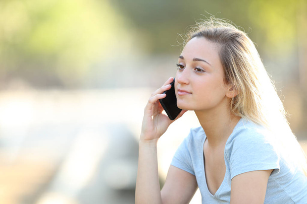 Serious teenage girl talking on phone in a park - Foto, afbeelding