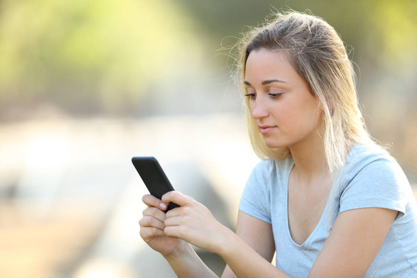 Serious teenage girl checking phone content in a park - Valokuva, kuva