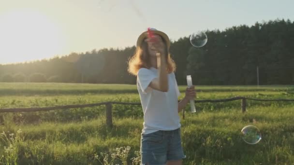 Beautiful girl teenager in a hat blowing soap bubbles - Filmati, video