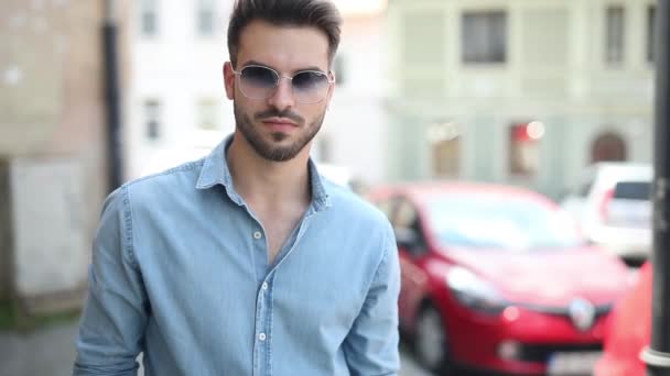 genç rahat adam eski bir şehrin sokakta poz, güneş gözlüğü ve mavi kot gömlek giyiyor - Video, Çekim