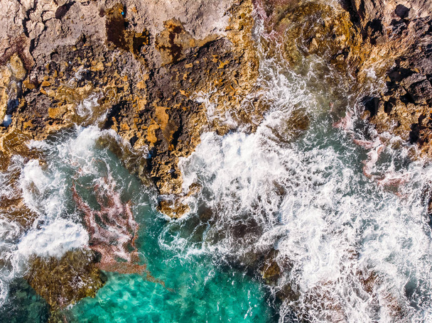 Top view Azure blue sea with waves beating on beach and rocks. Aerial photo. - Fotó, kép
