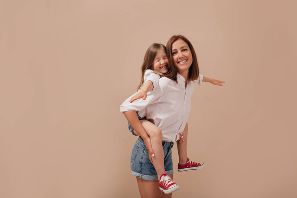Inspirowana młoda kobieta bez makijażu spędzać czas z córką, niosąc jej piggyback na białym tle. - Zdjęcie, obraz